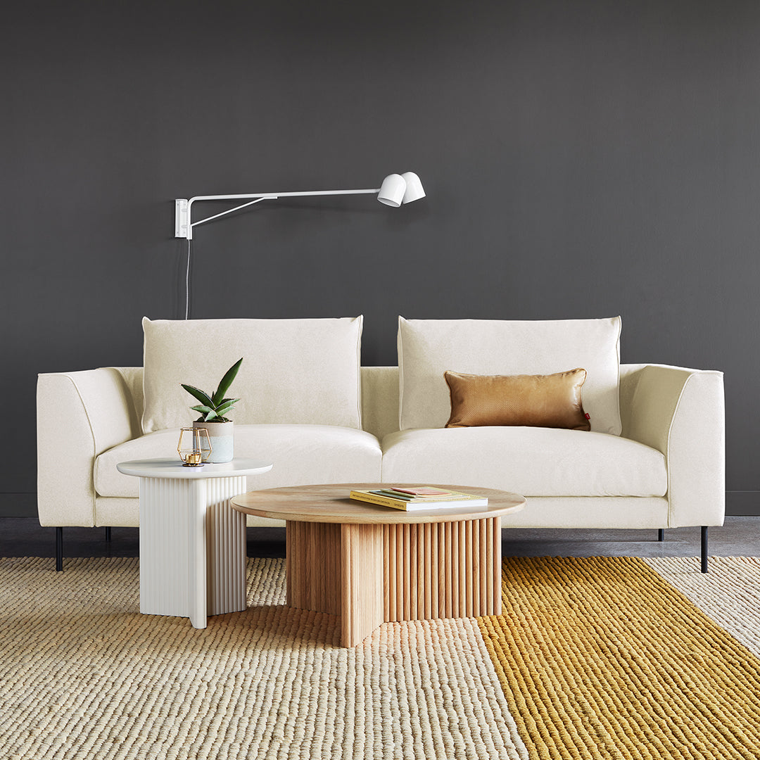 Beige sofa with a gold accent pillow, paired with a light wood coffee table on a striped beige and yellow rug.