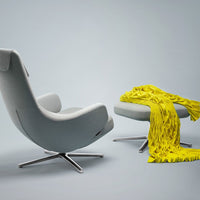 Gray modern chair and ottoman with a vibrant yellow fringed blanket draped over the ottoman against a light background.