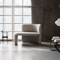 Modern beige upholstered chair with unique curved design against a minimalist grey backdrop. Soft, textured fabric.