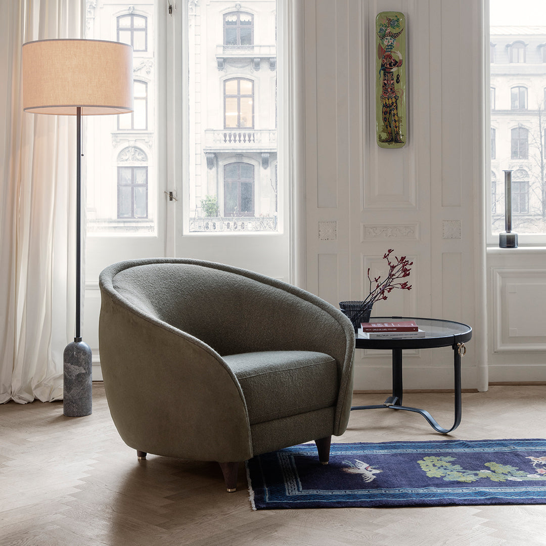 Olive green upholstered chair with subtle curved design, accented by a patterned blue rug and neutral-colored decor.