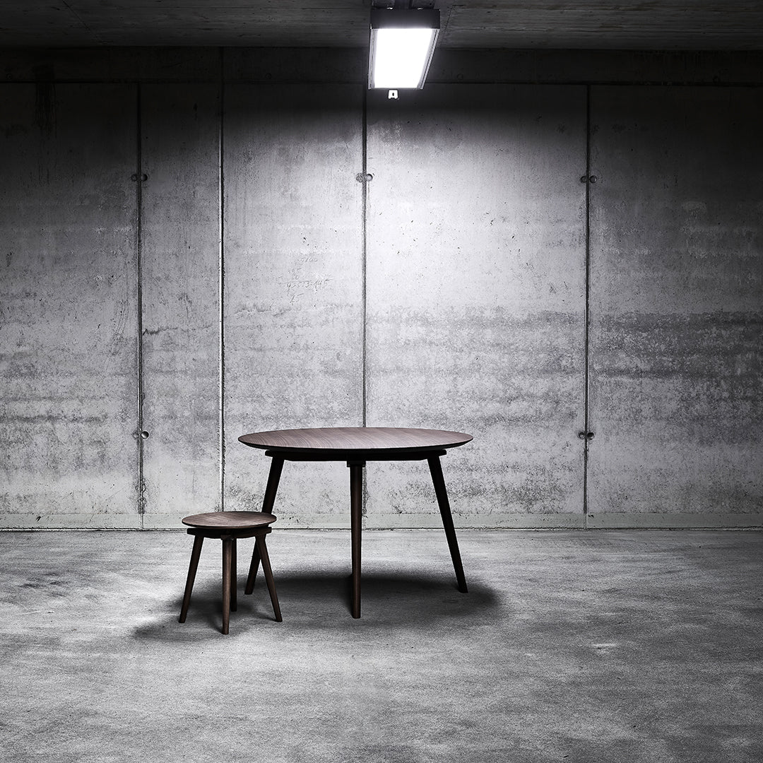 Round wooden table and chair in dark brown against a textured gray concrete background.