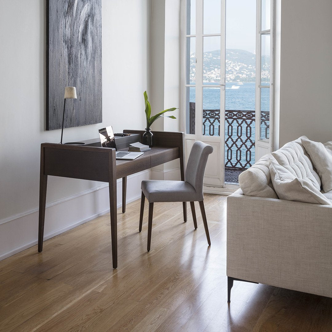 Light wood floor, gray chair, dark wood desk, cream sofa, and abstract black and white wall art with a coastal view.