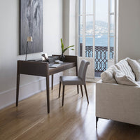 Light wood floor, gray chair, dark wood desk, cream sofa, and abstract black and white wall art with a coastal view.