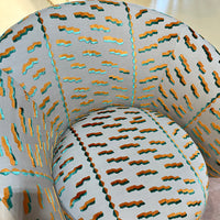 Colorful upholstered chair featuring teal, gold, and brown wave patterns on a light grey background.