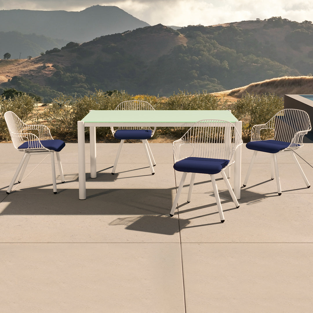 Modern white outdoor dining table with navy blue cushioned chairs against a scenic backdrop.
