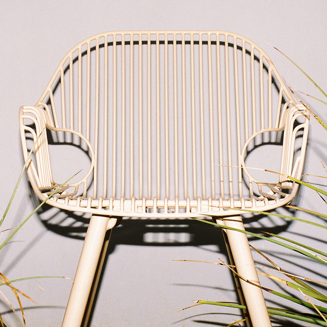Beige modern chair with sleek vertical line patterns and minimalistic design, surrounded by greenery.