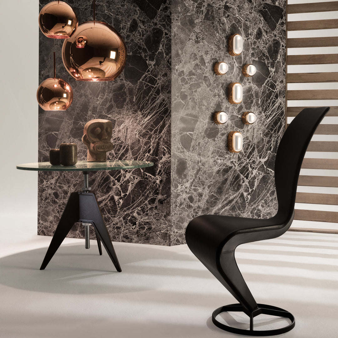 Modern black chair against a marble-patterned wall, featuring copper accents and a glass table, creating a stylish contrast.
