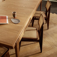 Natural oak table with woven cane chairs, featuring warm wood tones and minimalist design.
