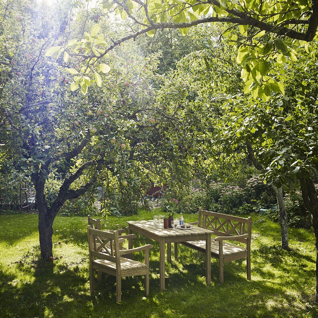 "Natural wood dining set in a lush green garden, accented by sunlight and vibrant foliage."