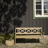 Light wood bench with cross pattern against a dark wood wall, complemented by a natural woven basket.