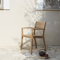Natural wood armchair in light beige with slatted pattern, set against a neutral stone background.