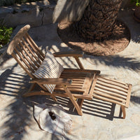 Natural wooden lounge chair with a striped cushion, casting patterned shadows on a stone patio.