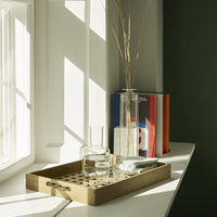 "Light wood tray with honeycomb pattern, clear glasses, and minimalist decor against a soft green background."