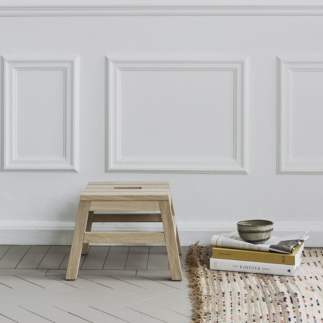 Light wood step stool with a natural finish, complemented by a textured woven rug and neutral-colored books.