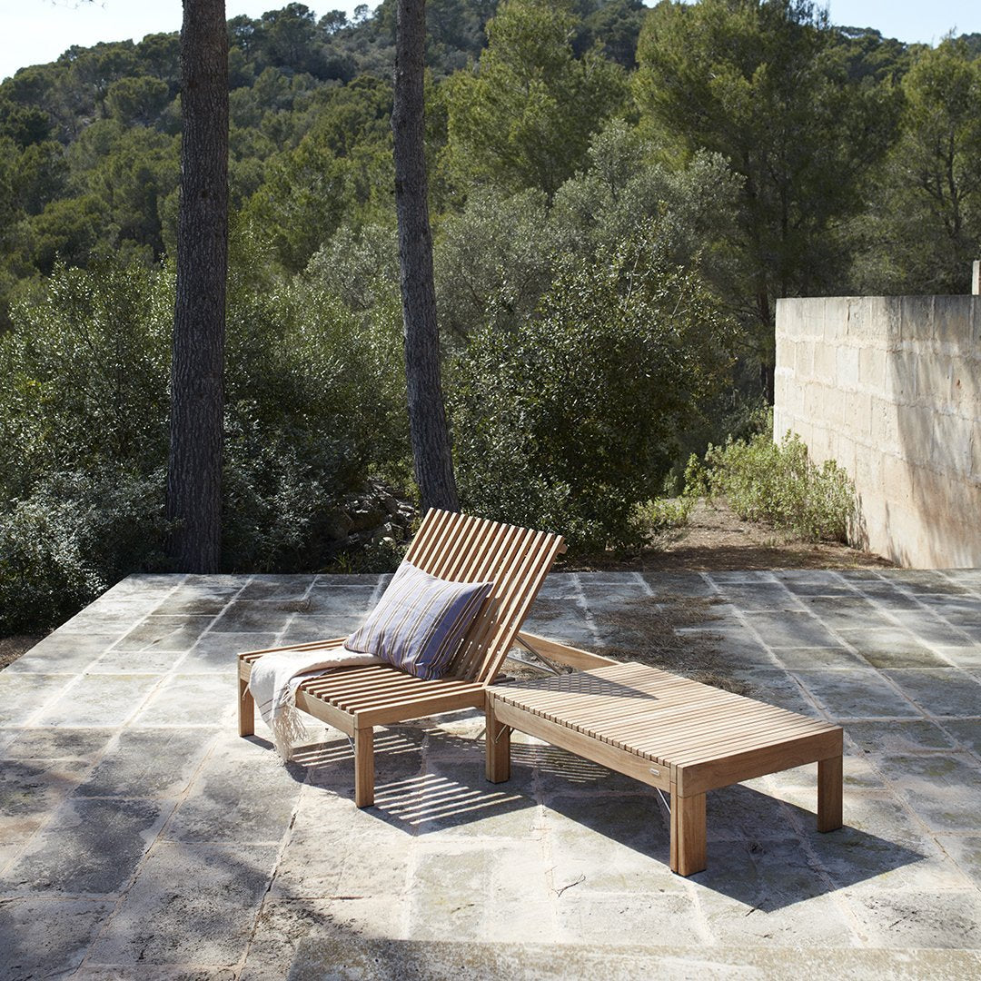 Wooden lounge chair with natural wood finish and striped cushion, set against a lush green landscape.