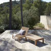 Wooden lounge chair with natural wood finish and striped cushion, set against a lush green landscape.