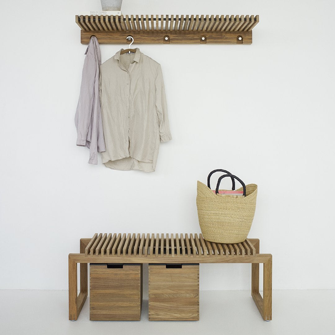 Wooden bench with slatted design, natural oak color, paired with neutral beige hanger and straw basket.