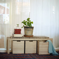 Wooden table with natural finish, striped top pattern, beige storage boxes, and blue fabric draped alongside a green plant.