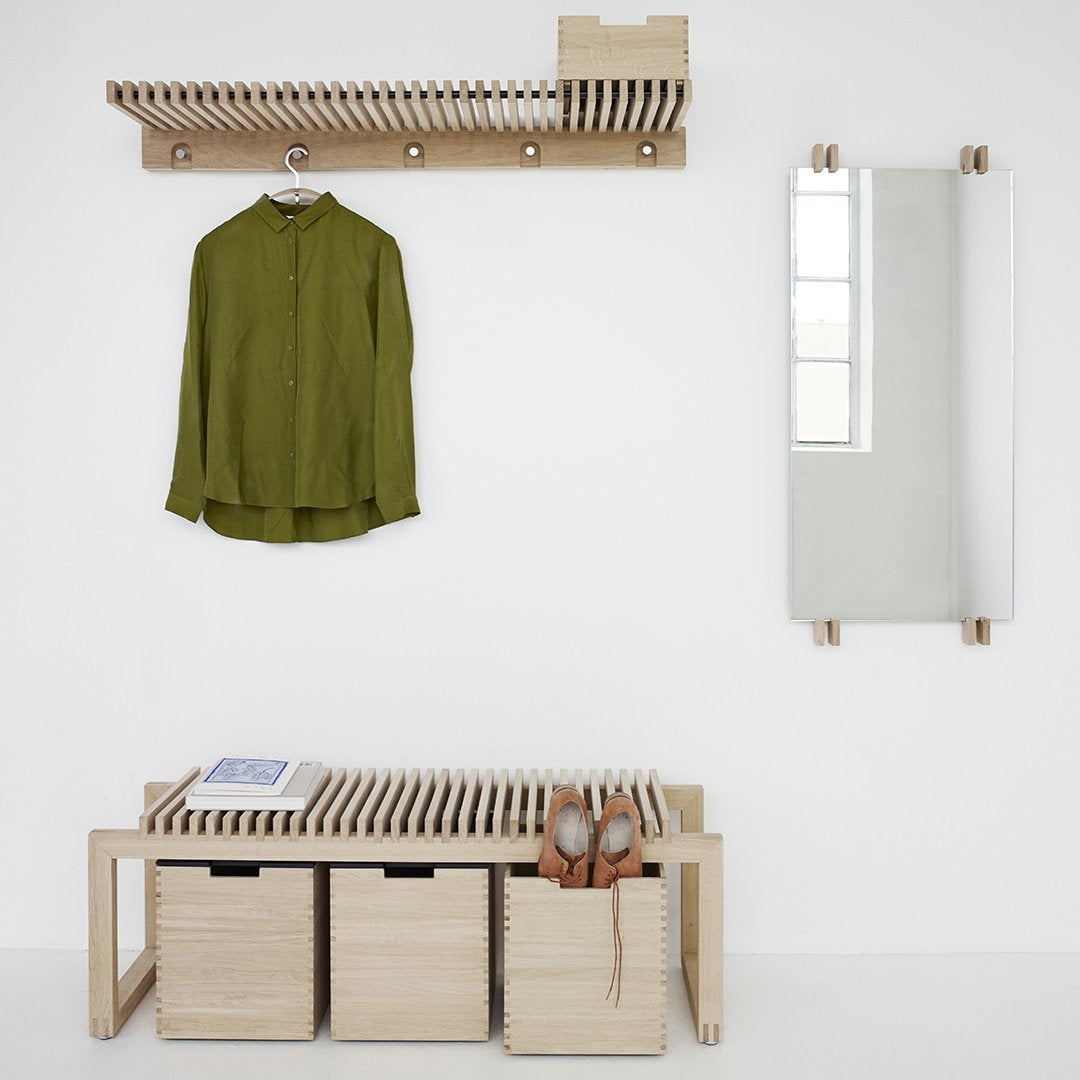 "Green button-up shirt on a wooden rack, light wood bench with woven pattern, and simple white backdrop."