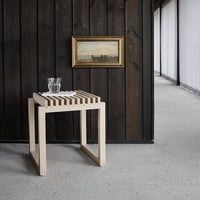 Light wood slatted table with a minimalist design, against a dark wooden wall. Clean, contemporary pattern.