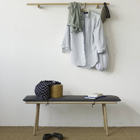 Gray bench with light wood legs, featuring navy polka dot bag and beige woven basket. Casual, minimalist decor.