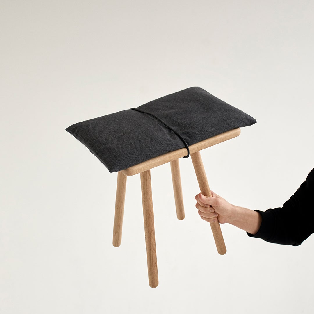 Black cushion on a light wood stool, featuring a minimalist design and natural tones. Ideal for modern decor.