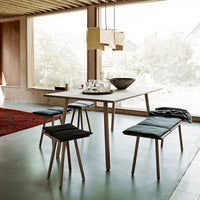 Modern dining table and benches with natural wood finish and dark cushions, accented by a vibrant red rug.