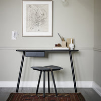 Modern black desk with sleek lines, complemented by a patterned rug in warm tones, set against a neutral grey wall.