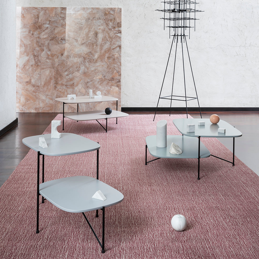 Modern tables in soft gray, featuring sleek lines, set on a textured pink rug against a neutral backdrop.
