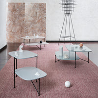Modern tables in soft gray, featuring sleek lines, set on a textured pink rug against a neutral backdrop.
