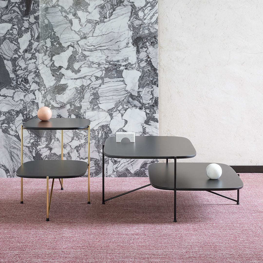 Black and gold geometric tables on pink carpet against a textured gray and white wall. Modern and stylish design.