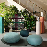 Turquoise and teal poufs on a textured rug, surrounded by green plants, neutral-colored sculptures, and colorful vertical storage.