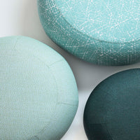 Textured round ottomans in light aqua, teal, and dark green hues with abstract patterns. Perfect for stylish decor.