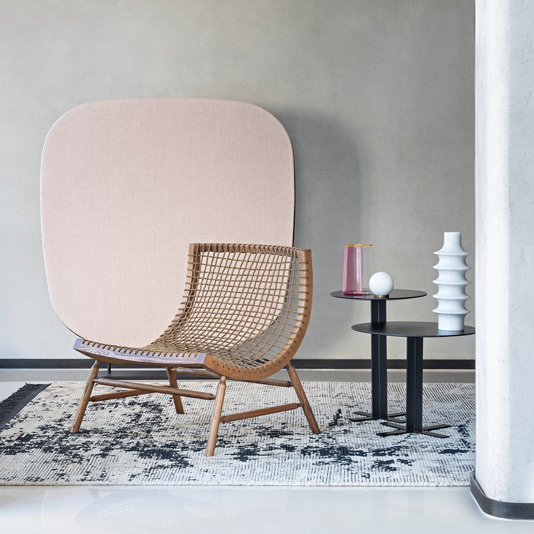 Woven rattan chair with natural wood tones, complemented by a soft pink backdrop and geometric patterned rug.