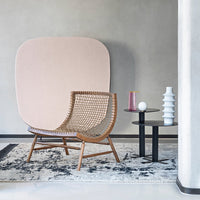 Woven rattan chair with natural wood tones, complemented by a soft pink backdrop and geometric patterned rug.