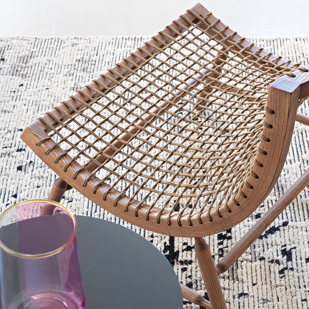 Woven rattan stool in natural wood tones, featuring a chic grid pattern, with a vibrant pink glass on a black table.