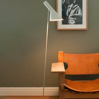 Modern silver floor lamp with a sleek design, set against a muted green wall and complemented by a warm tan chair.