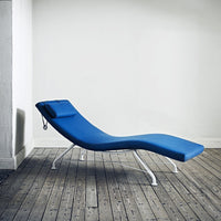 Blue lounge chair with sleek lines and a smooth finish, set against a minimalist backdrop and wooden floor.