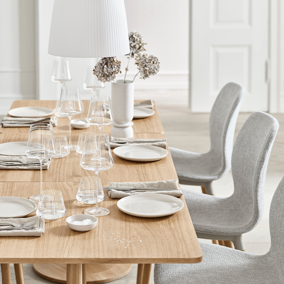 Elegant wooden dining table setting with neutral gray and white tones, featuring smooth glassware and textured napkins.