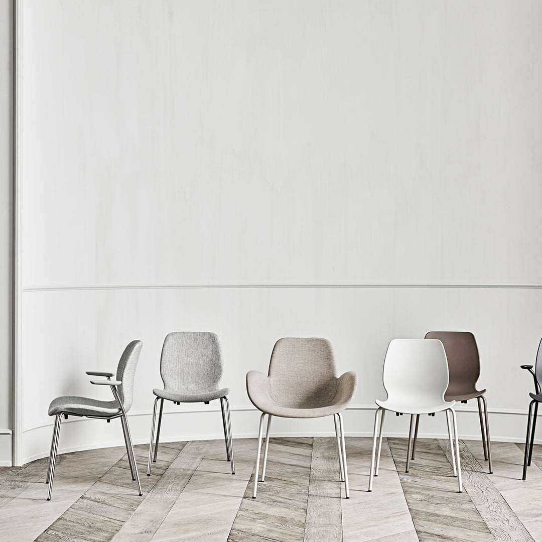 Assorted modern chairs in gray, beige, white, and black on a light wood floor with a minimalist backdrop.