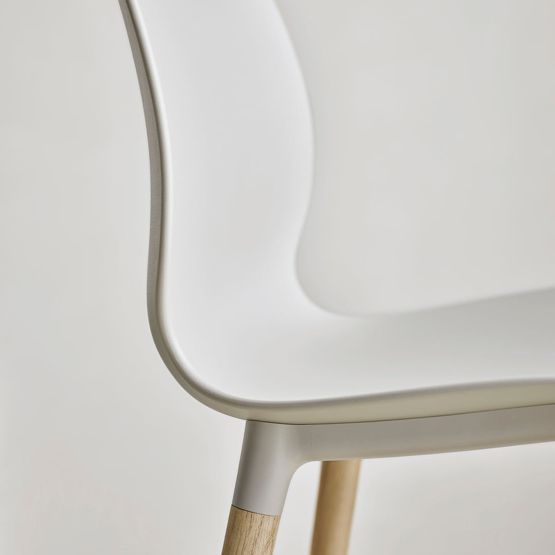 White chair with smooth, curved design and light wood legs, featuring minimalistic and modern aesthetics.