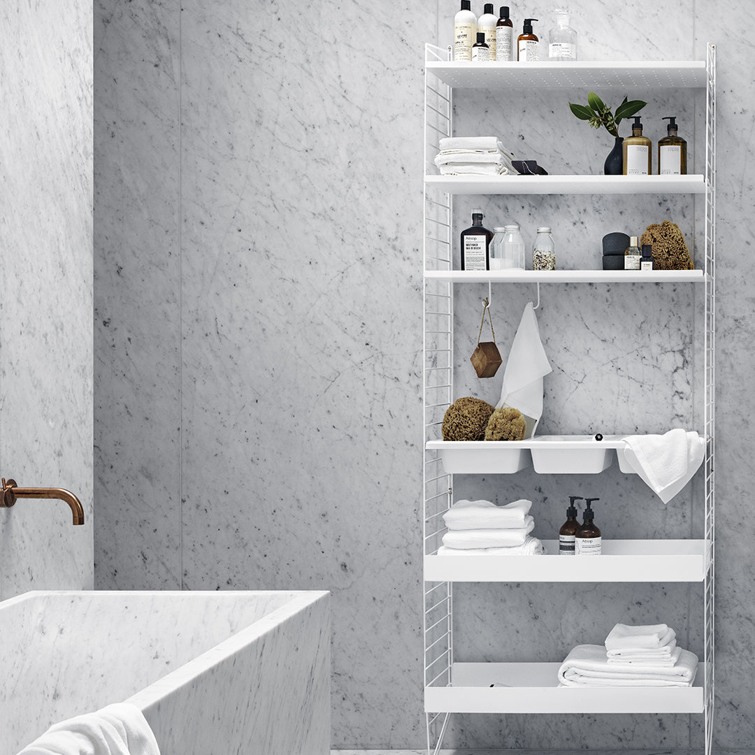 Modern white shelving unit against a textured gray marble wall, showcasing towels and decorative items.