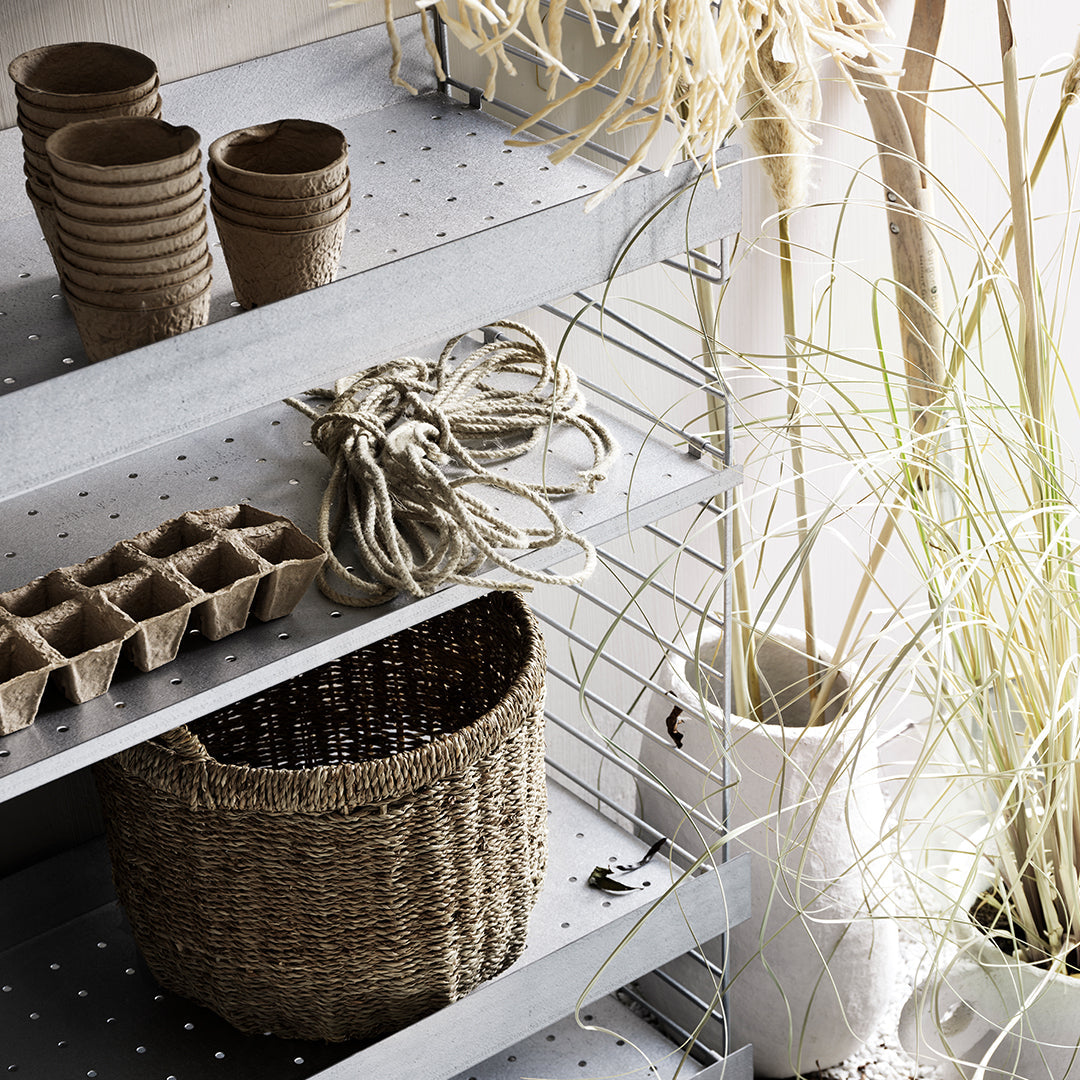 Natural woven basket, neutral tones, earthy clay pots, soft textures, and green plant accents on metal shelves.