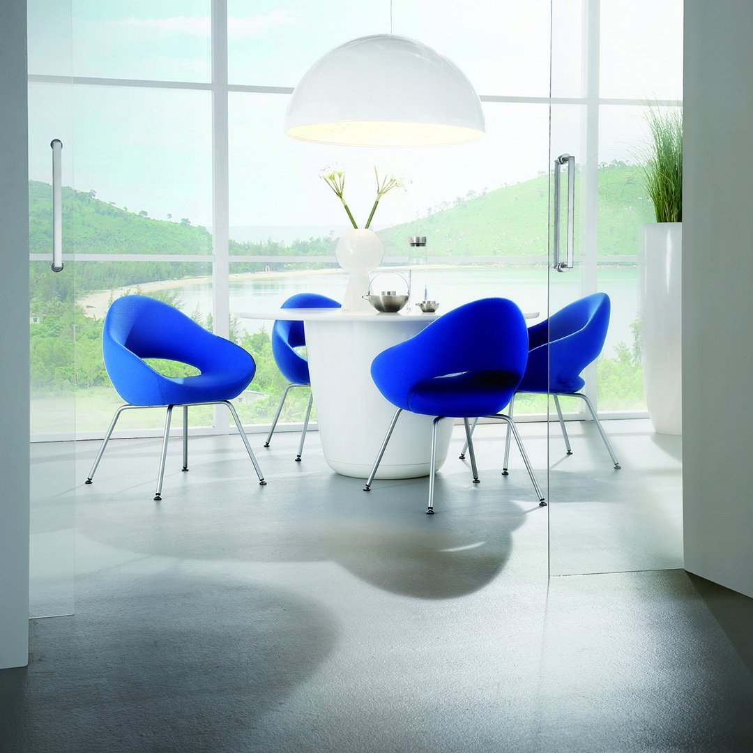 Bright blue chairs surround a sleek white table, set against a serene green landscape and large windows.