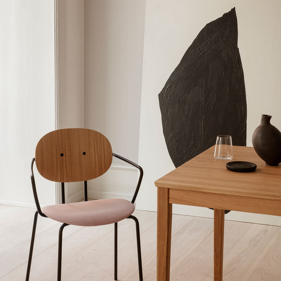 Wooden chair with pink cushion, sleek black accents, and simple wooden table in a neutral-toned interior setting.