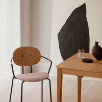 Wooden chair with pink cushion, sleek black accents, and simple wooden table in a neutral-toned interior setting.