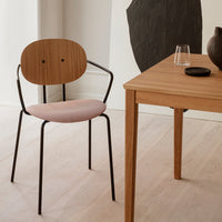 Pink upholstered chair with a natural wood backrest and black metal frame, set against a minimalist background.