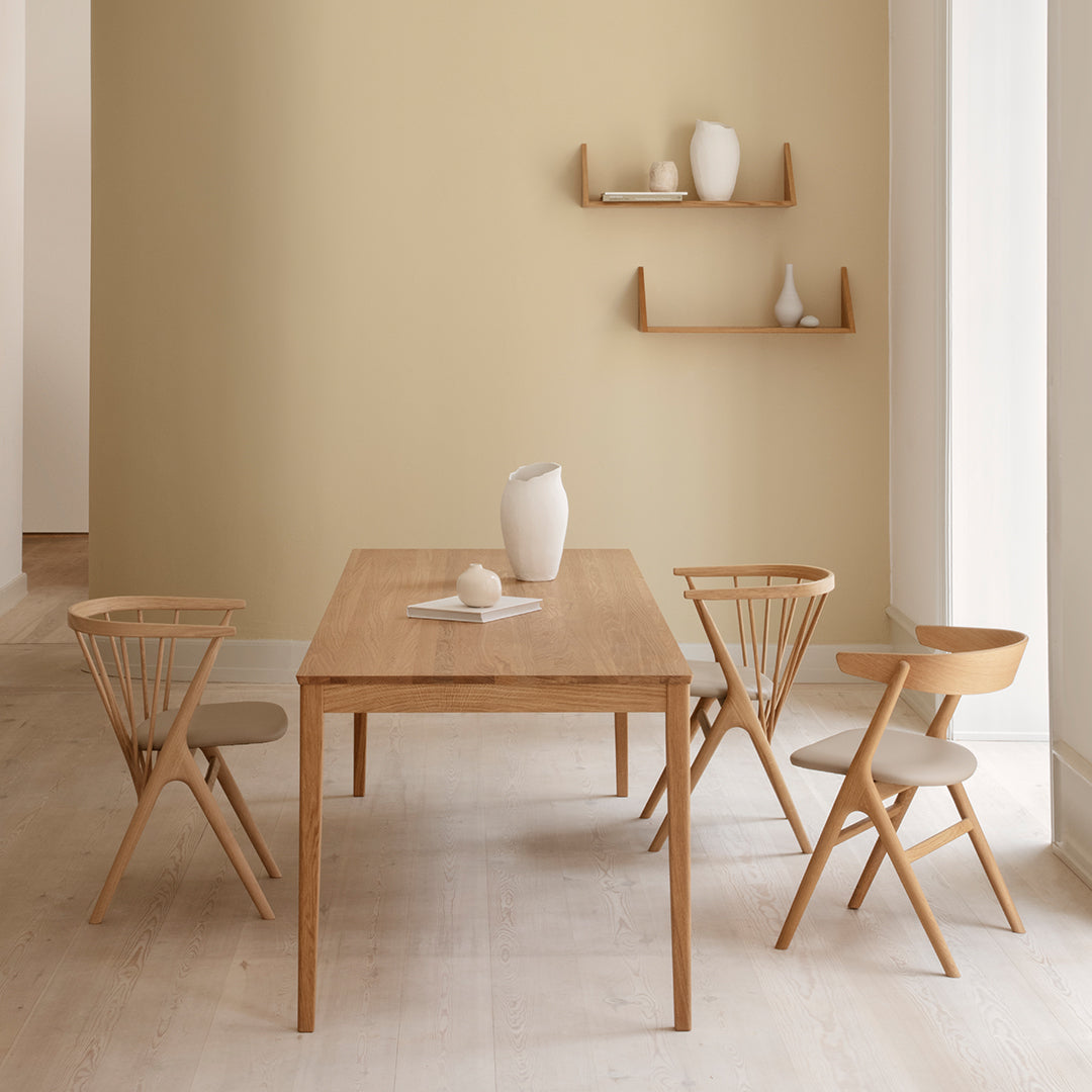 Light wood dining table with beige walls and natural wood chairs featuring light upholstery. Minimalist, modern decor.