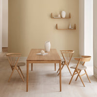 Light wood dining table with beige walls and natural wood chairs featuring light upholstery. Minimalist, modern decor.