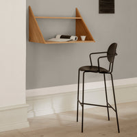 Wooden wall shelf in warm oak finish against a soft gray wall, complemented by a sleek black metal chair.
